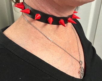 Könnte beinhalten: Ein schwarzer Leder-Choker mit roten Spikes. Der Choker wird um den Hals einer Person getragen.