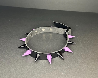 May include: A black leather choker with purple spikes. The choker has a buckle closure and is adjustable.