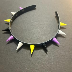 May include: A black headband with eight spikes in different colors: purple, white, yellow, and black. The headband is made of a flexible material and is designed to be worn around the head.