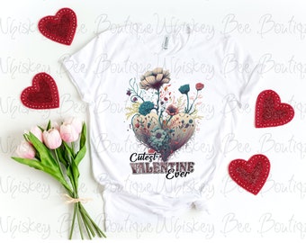 Könnte beinhalten: Weißes T-Shirt mit einem floralen Herzdesign und dem Text "Cutest Valentine Ever".