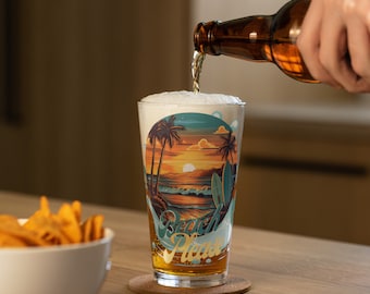 May include: A clear glass with a beach scene and the text "Beach Please" is being filled with beer from a brown bottle.