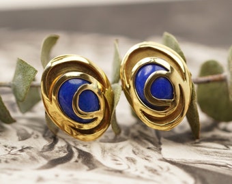 Könnte beinhalten: Ein Paar goldene Ohrringe mit blauen Edelstein-Akzenten. Die Ohrringe sind oval geformt und haben ein Wirbeldesign.