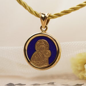 May include: Gold pendant necklace featuring a round pendant with a blue center and a gold religious icon. The pendant hangs from a gold-colored cord. The icon depicts a religious figure holding a child.