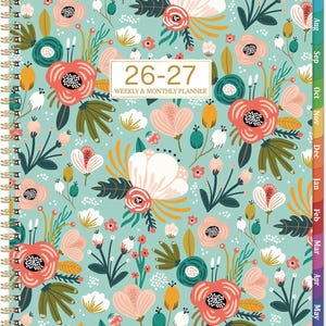 May include: A floral weekly and monthly planner with a teal background and a gold spiral binding. The cover features a repeating pattern of flowers in shades of pink, coral, white, and green. The text "26-27 WEEKLY & MONTHLY PLANNER" is displayed on the cover.