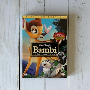 May include: A DVD case for Disney's "Bambi" 2-Disc Special Edition. The cover features Bambi, a butterfly, Thumper, and Flower. The case has a gold border and the words "Platinum Edition" at the top. A gold sticker reads "First Time Ever On DVD Limited Time Only".