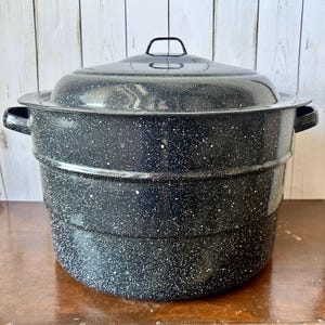 May include: A large, speckled black enamel canning pot with a matching lid. The pot has two side handles and a handle on the lid. The pot is sitting on a wooden surface.