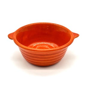 May include: An orange ceramic bowl with a ribbed exterior and two small handles. The bowl has a glossy finish and is set against a white background. This kitchenware item is suitable for serving soups, stews, or side dishes.