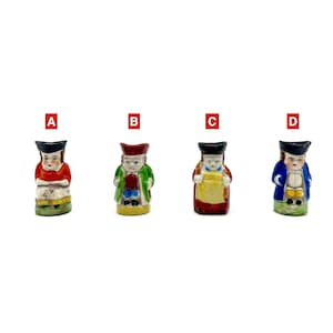 May include: Four small, vintage ceramic figurines of people in traditional attire. Each figurine is painted with different colors, including red, green, blue, and yellow. The figurines are labeled A, B, C, and D.