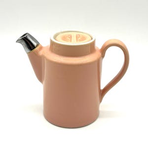 May include: A pink ceramic teapot with a silver lid and a silver spout. The teapot has a rounded body and a handle on the side.