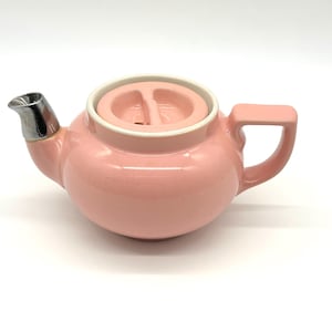 May include: A pink ceramic teapot with a silver spout and lid. The lid has a built-in strainer.