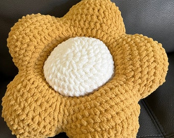 May include: A handmade, flower-shaped pillow with a textured, chunky knit design. The petals are a warm, golden-brown color, and the center is a soft, off-white. This decorative pillow adds a touch of whimsy to any room.