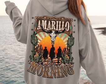 May include: A gray hoodie with a vintage-style graphic on the back. The graphic features a sunset, cacti, and three cowboys riding horses. The text "Amarillo By Morning" is printed below the graphic.