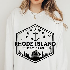 May include: White sweatshirt with a black graphic design featuring a lighthouse, a ship, an anchor, and the text "RHODE ISLAND -EST. 1790- ".