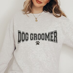 May include: A heather gray sweatshirt with the text "DOG GROOMER" in black with a paw print below.