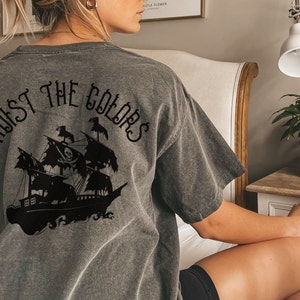 May include: A gray t-shirt with a black graphic of a pirate ship and the text "Hoist the Colors" on the back.