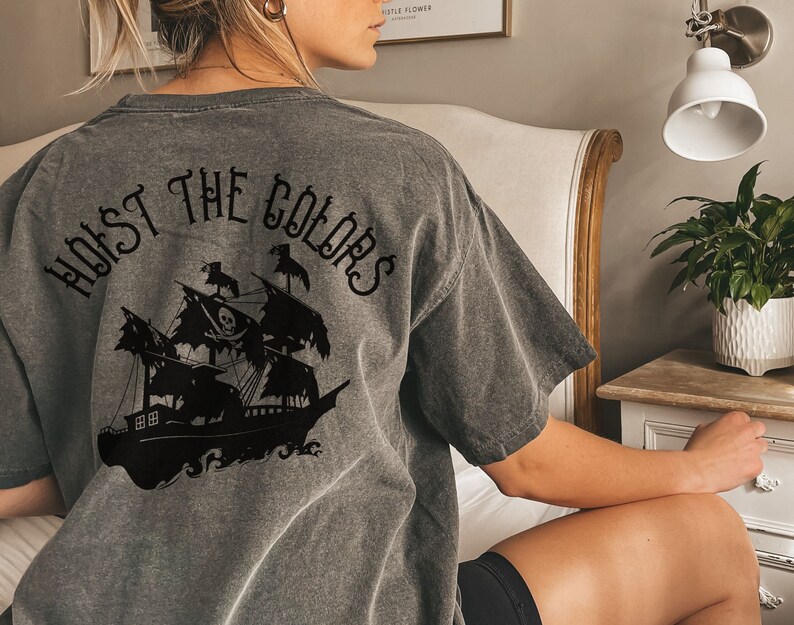 May include: A gray t-shirt with a black graphic of a pirate ship and the text "Hoist the Colors" on the back.