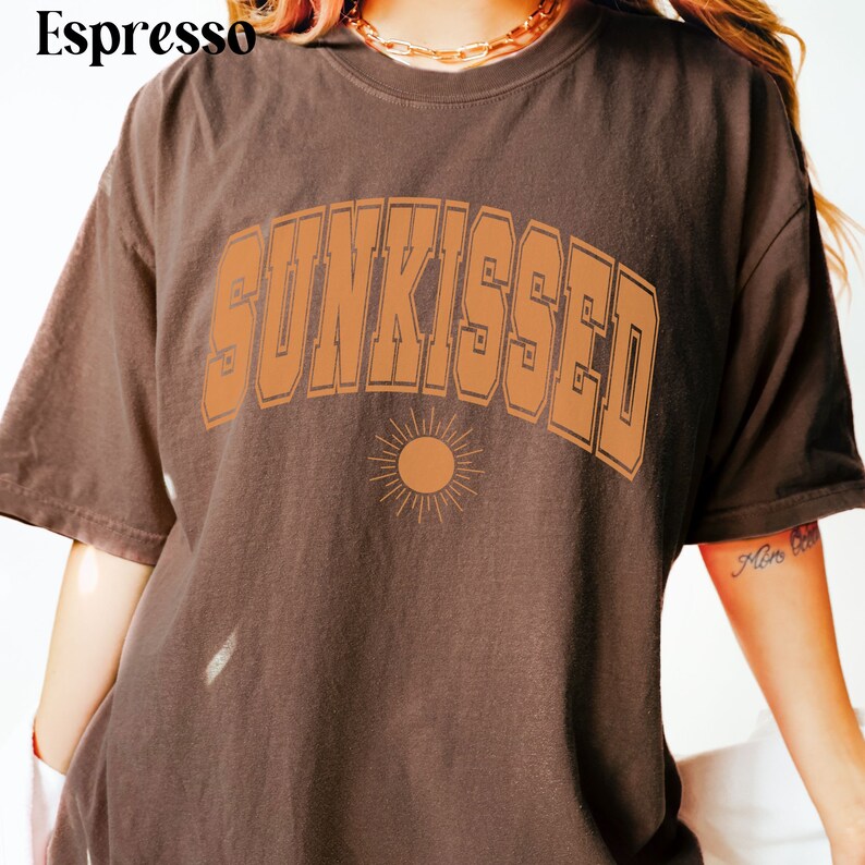 May include: A brown t-shirt with the text "SUNKISSED" in orange letters with a stylized sun graphic below.
