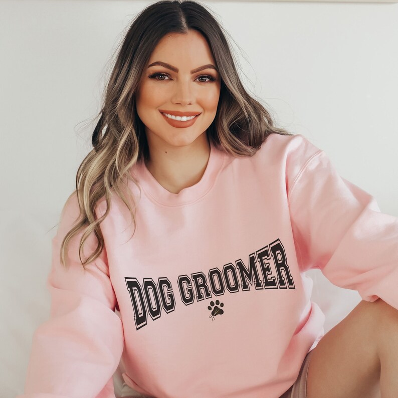 May include: A pink sweatshirt with the text "DOG GROOMER" in black block letters with a paw print below.