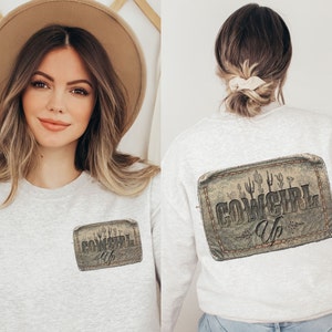 May include: A gray sweatshirt with a distressed brown patch on the front and back that says "COWGIRL Up" with cactus silhouettes.