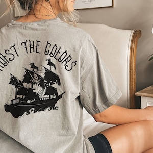 May include: A gray t-shirt with a black graphic of a pirate ship and the text "HOIST THE COLORS" on the back.