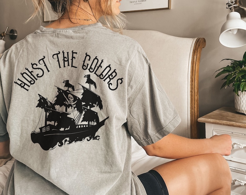 May include: A gray t-shirt with a black graphic of a pirate ship and the text "HOIST THE COLORS" on the back.