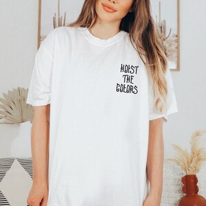 May include: White oversized t-shirt with black text that reads "HOIST THE COLORS" on the front.