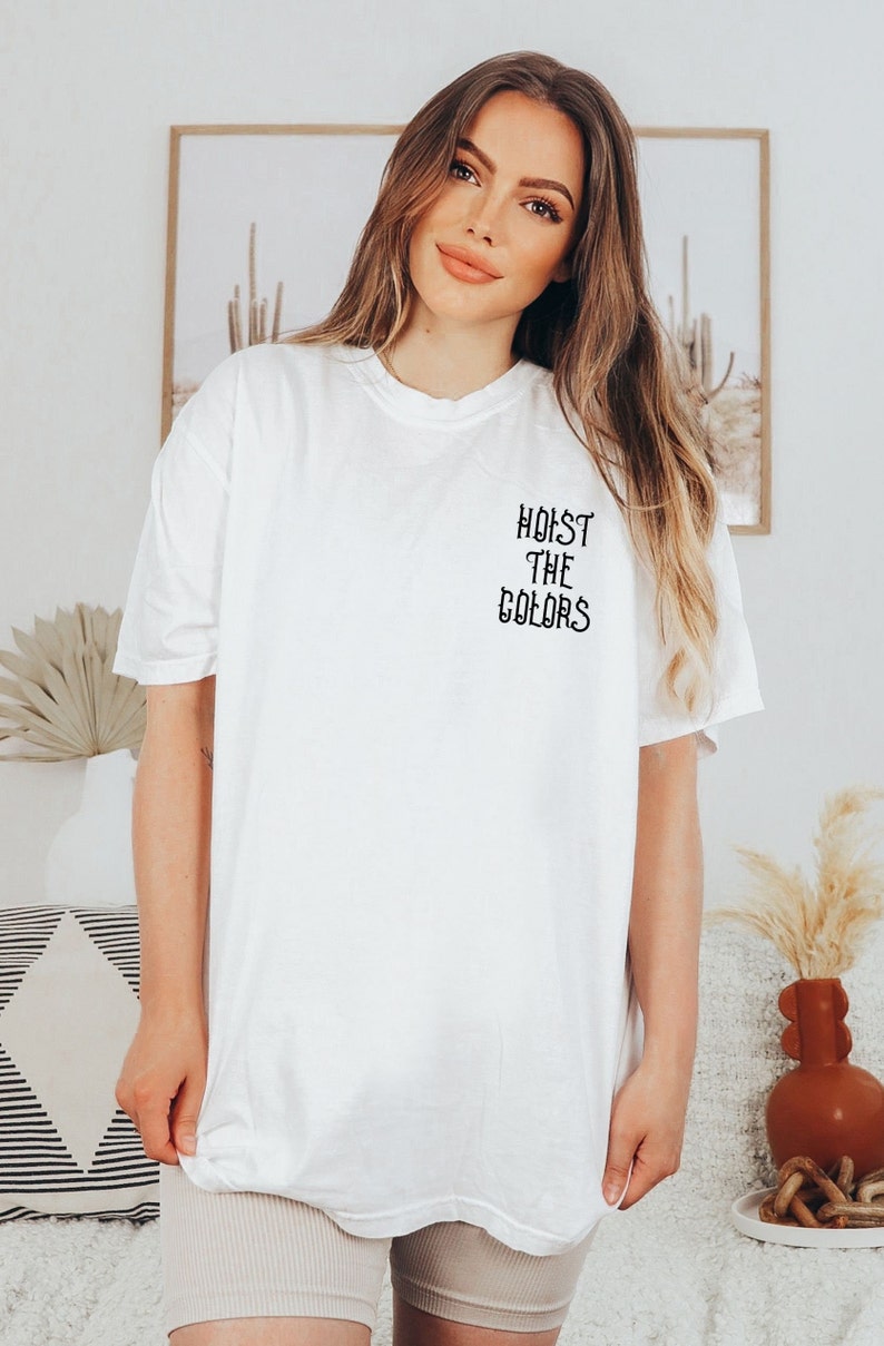 May include: White oversized t-shirt with black text that reads "HOIST THE COLORS" on the front.