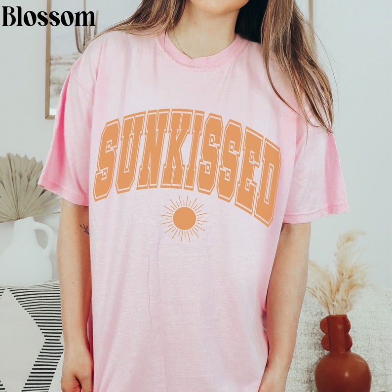 May include: A pink t-shirt with the word "SUNKISSED" in orange letters with a stylized sun graphic below.