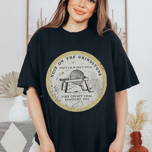 May include: Black oversized t-shirt with a vintage-style graphic of a grindstone with the text "Nose on the Grindstone Don't Lie & Don't Steal Pike County Coal Kentucky, USA".