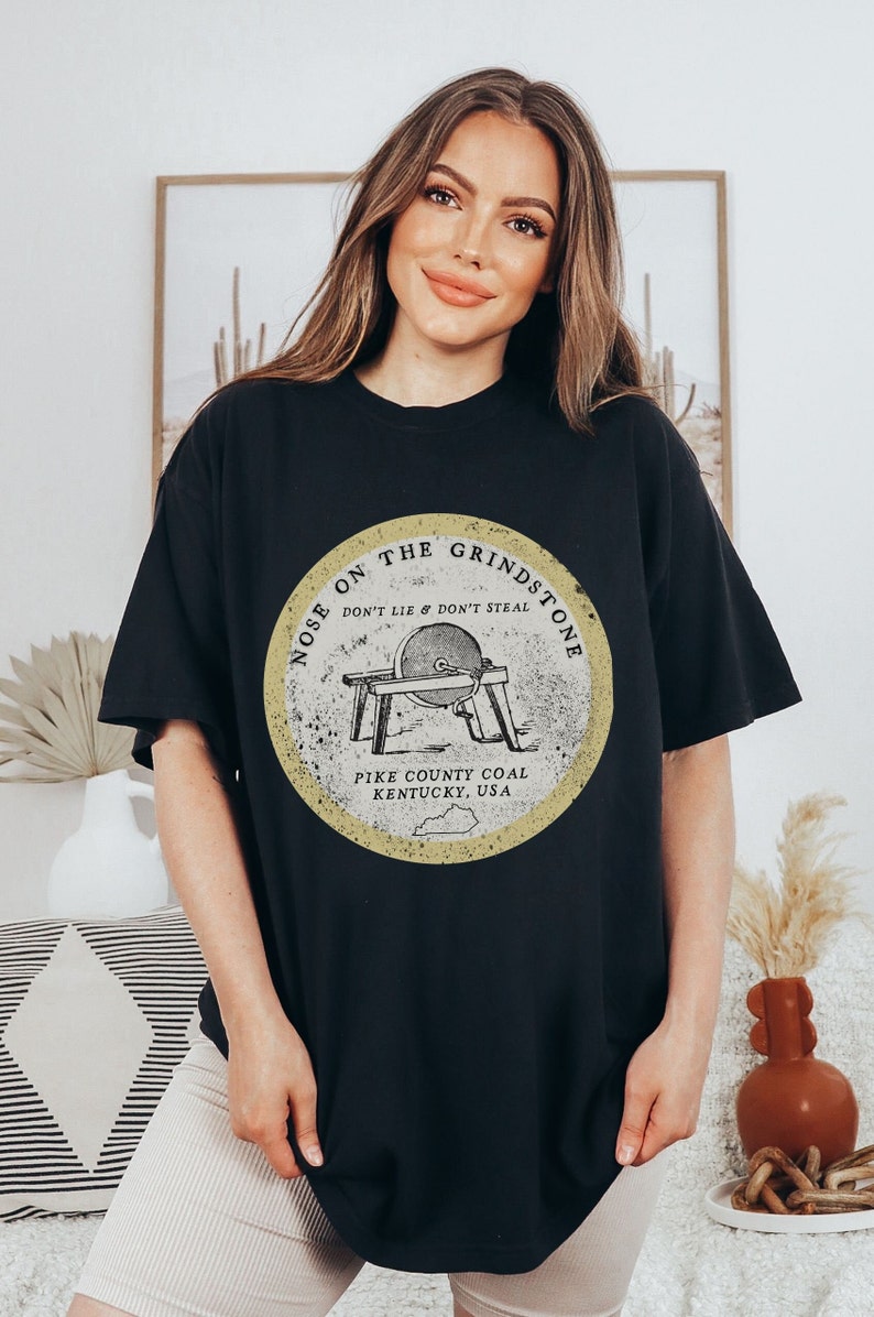May include: Black oversized t-shirt with a vintage-style graphic of a grindstone with the text "Nose on the Grindstone Don't Lie & Don't Steal Pike County Coal Kentucky, USA".