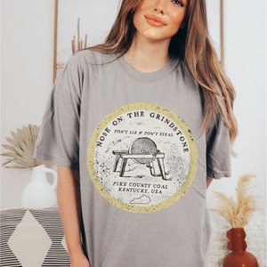 May include: Gray t-shirt with a yellow circle graphic featuring a grindstone with the text "Nose on the Grindstone Don't Lie & Don't Steal Pike County Coal Kentucky, USA".