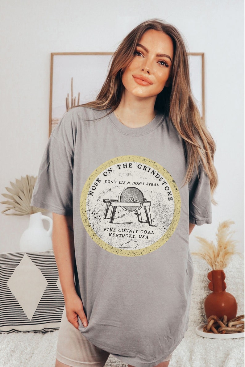 May include: Gray t-shirt with a yellow circle graphic featuring a grindstone with the text "Nose on the Grindstone Don't Lie & Don't Steal Pike County Coal Kentucky, USA".