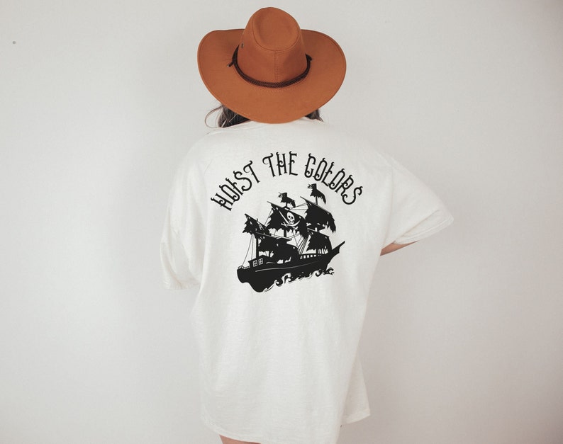 May include: White t-shirt with a black silhouette of a pirate ship and the text "Hoist the Colors" on the back.
