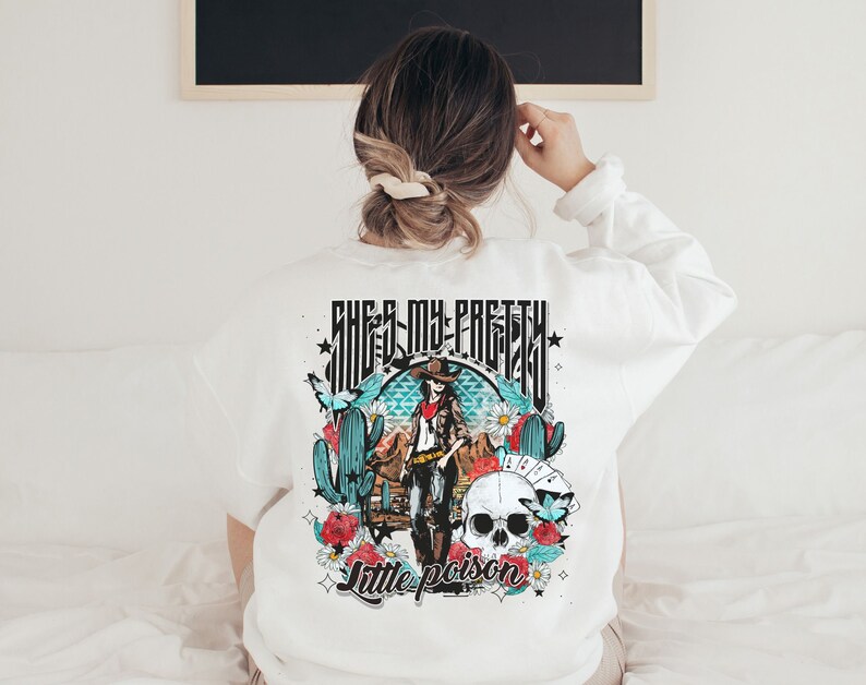 May include: White sweatshirt with a graphic print of a woman in a cowboy hat and a skull with flowers and cacti. The text "She's my pretty little poison" is printed below the graphic.