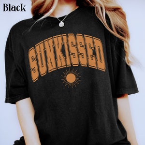 May include: A black t-shirt with a brown graphic that says "SUNKISSED" in a retro font with a stylized sun underneath.