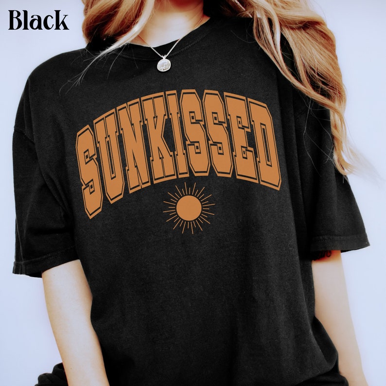 May include: A black t-shirt with a brown graphic that says "SUNKISSED" in a retro font with a stylized sun underneath.