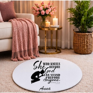Puede incluir: Una alfombra redonda de color blanco que presenta la silueta negra de una persona arrodillada y el texto "She who kneels before God can stand before anyone. Romans 8:31" junto al nombre "Anna" impreso en letras negras sobre la superficie.