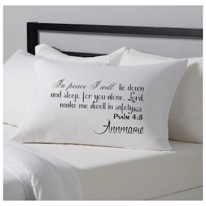 May include: White pillowcase with black text that reads "In peace I will lie down and sleep, for you alone, Lord, make me dwell in safety. Psalm 4:8 Annmarie." The pillow is on a bed with white sheets.