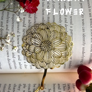 May include: A gold metal bookmark shaped like a dahlia flower. The bookmark is on top of an open book with text about career guidance and education.