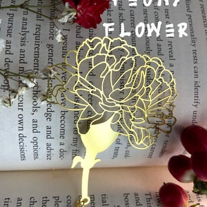 May include: A gold metal bookmark shaped like a peony flower. The bookmark is on top of a book with text about career counseling and standardized personality tests.