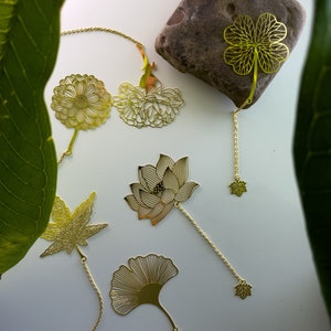 May include: A set of six gold-toned metal bookmarks featuring various floral and leaf designs. The bookmarks are attached to chains with small decorative charms at the ends.