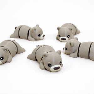 May include: Five articulated bear figurines in a light gray color. Each bear features a smooth, rounded head with black eyes, a white muzzle, and a dark brown nose. The bodies are segmented into three parts, allowing for movement, with small ears.