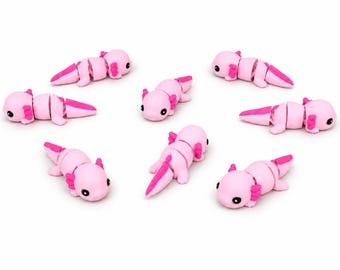 May include: A collection of seven small, articulated axolotl figurines. Each figurine is light pink with darker pink accents on the gills and tail, featuring black eyes and a segmented body design that allows for movement and flexibility.