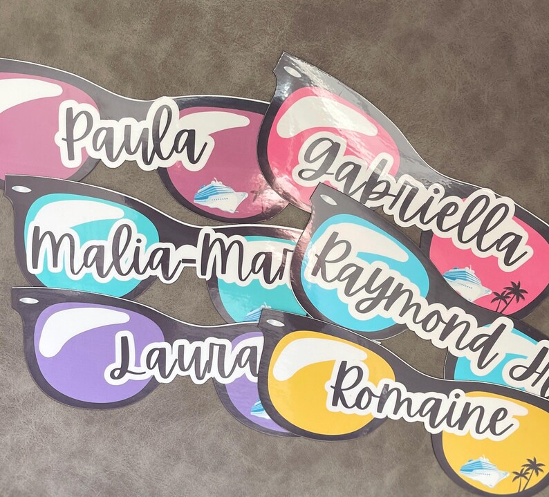 Puede incluir: Una colecci&oacute;n de pegatinas troqueladas con forma de gafas de sol, cada una con un nombre &uacute;nico en letra blanca: Paula, Gabriella, Malia-Marie, Raymond, Laura y Romaine. Las lentes muestran colores vibrantes, iconos de cruceros y palmeras.