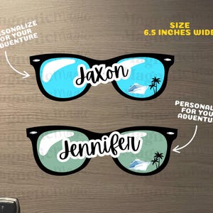Puede incluir: Dos pegatinas de gafas de sol con montura negra, de 16,51 cm de ancho, con lentes azules y verdes que reflejan un crucero y palmeras. Los nombres Jaxon y Jennifer est&aacute;n impresos en letra cursiva blanca en el centro de cada par.