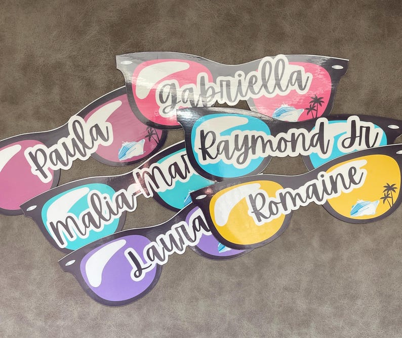 Puede incluir: Una colecci&oacute;n de gafas de sol de papel troquelado con varios nombres, incluidos Gabriella, Paula, Raymond Jr, Malia-Mari, Laura y Romaine. Cada par muestra un dise&ntilde;o de lente colorido con una ilustraci&oacute;n gr&aacute;fica de un crucero y palmeras.
