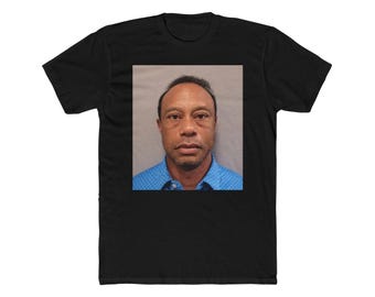 May include: Black t-shirt with a square image of a man in a blue collared shirt. The image is a mugshot. The t-shirt is made of a soft material and has short sleeves.