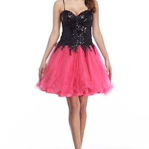 May include: A short, strapless dress with a black sequined bodice and a bright pink tulle skirt. The dress features a sweetheart neckline and delicate spaghetti straps. The model is wearing beige heels.