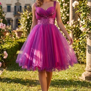 May include: A knee-length dress in vibrant shades of magenta and purple, featuring a sweetheart neckline, wide straps, and a fitted bodice adorned with shimmering sequins. The skirt is crafted from multiple layers of sheer tulle fabric.