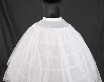 Puede incluir: Un miriñaque blanco con múltiples aros, exhibido en un maniquí negro. El miriñaque tiene una forma completa y redonda, con un delicado ribete de encaje a lo largo del dobladillo. La tela parece ser un material ligero y transparente.